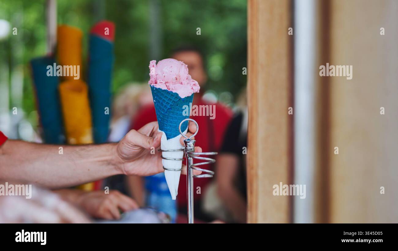 Ein Eisverkäufer schöpft Eis in bunte Waffelkegel. Stockfoto