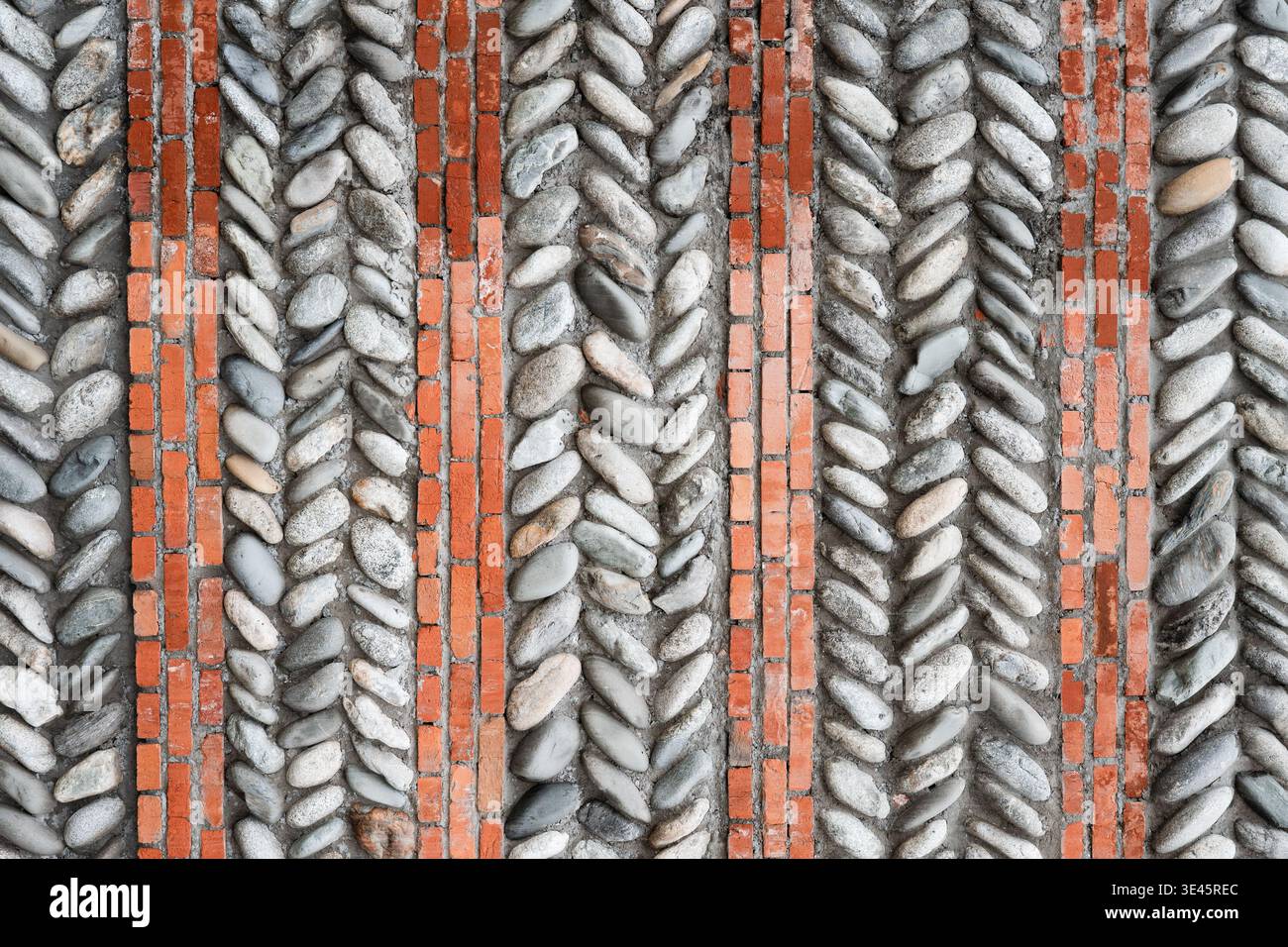 Pflastermuster aus Kieselstein und rotem Backstein in Fischgrätendesign, architektonische Hintergrundstruktur. Stockfoto