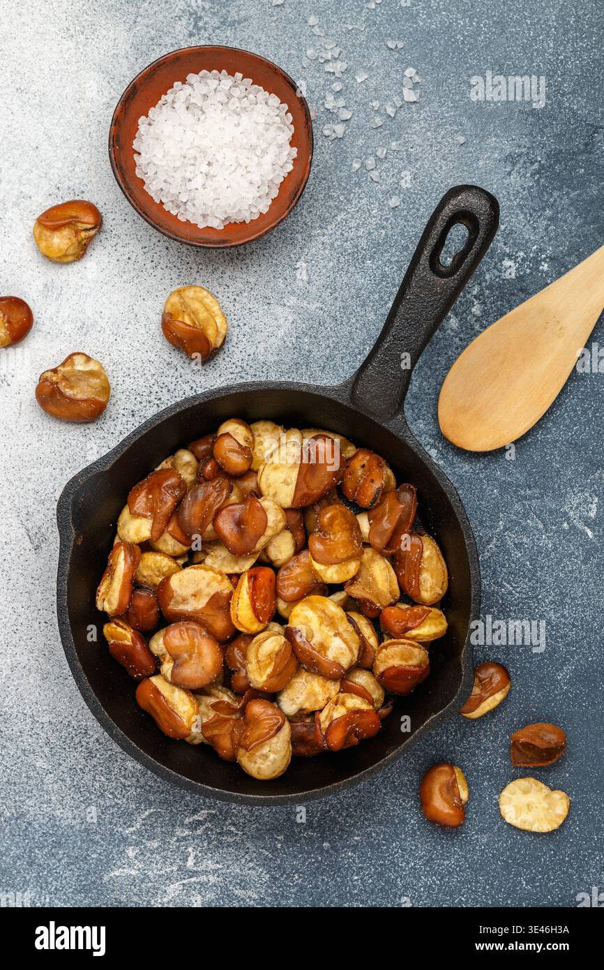 Knusprig gebratene breite Bohnen mit Salz in einer gusseisernen Pfanne Nahaufnahme auf grauem Betonhintergrund. Bier-Snack. Vicia Faba. Trockene Fava-Bohnen bereit für E Stockfoto