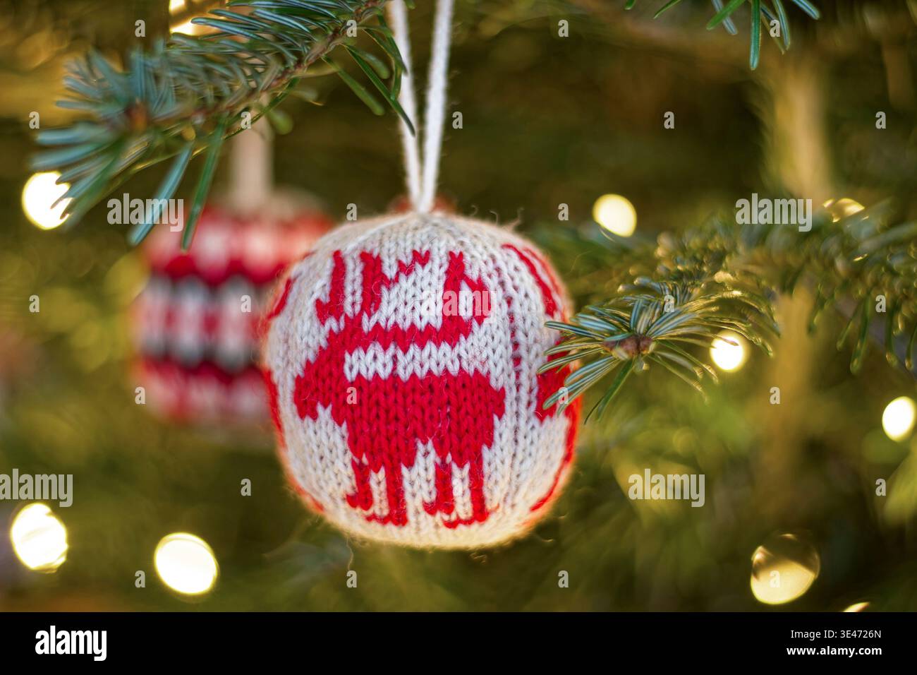 Handgestrickte Weihnachtskugeln auf einem beleuchteten Weihnachtsbaum Stockfoto