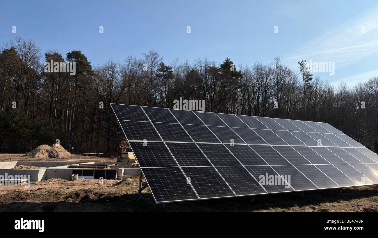 Installation von Solarpaneelen auf einer Baustelle in der Nähe des Waldes, erneuerbare Energien für Öko-Haus, Photovoltaik-Module, nachhaltiges Gebäude - Smartphone-aufgenommenes Stockfoto