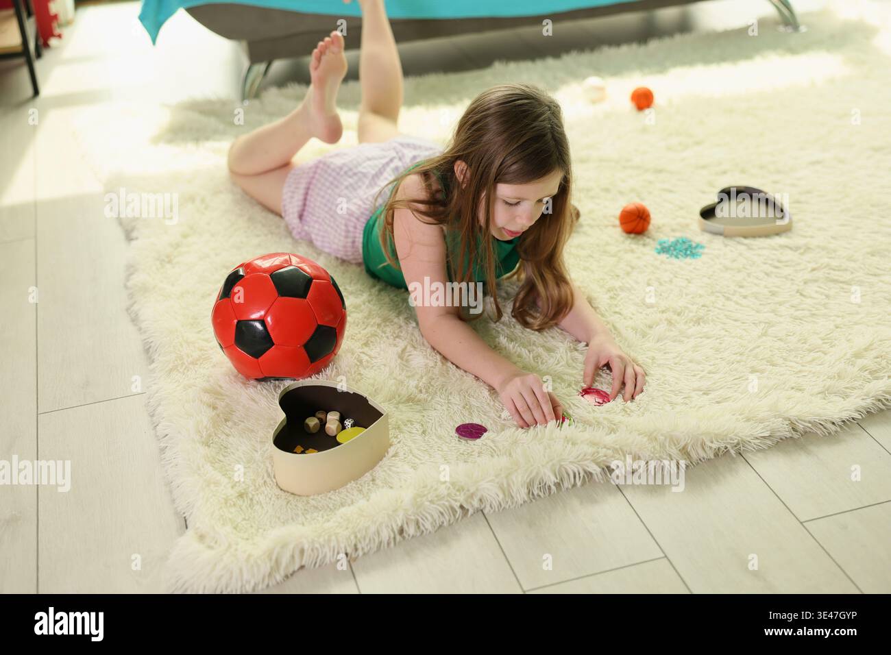 Mädchen genießt spielerische Momente in Innenräumen, während sie bunte Gegenstände auf einem weichen Teppich sortieren, umgeben von lebendigen Spielzeugen Stockfoto