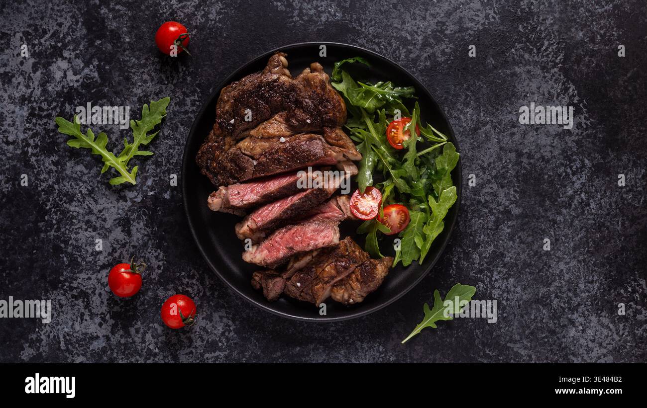 Gegrilltes Rindersteak mit Gewürzen auf schwarzem Teller, Draufsicht. Stockfoto