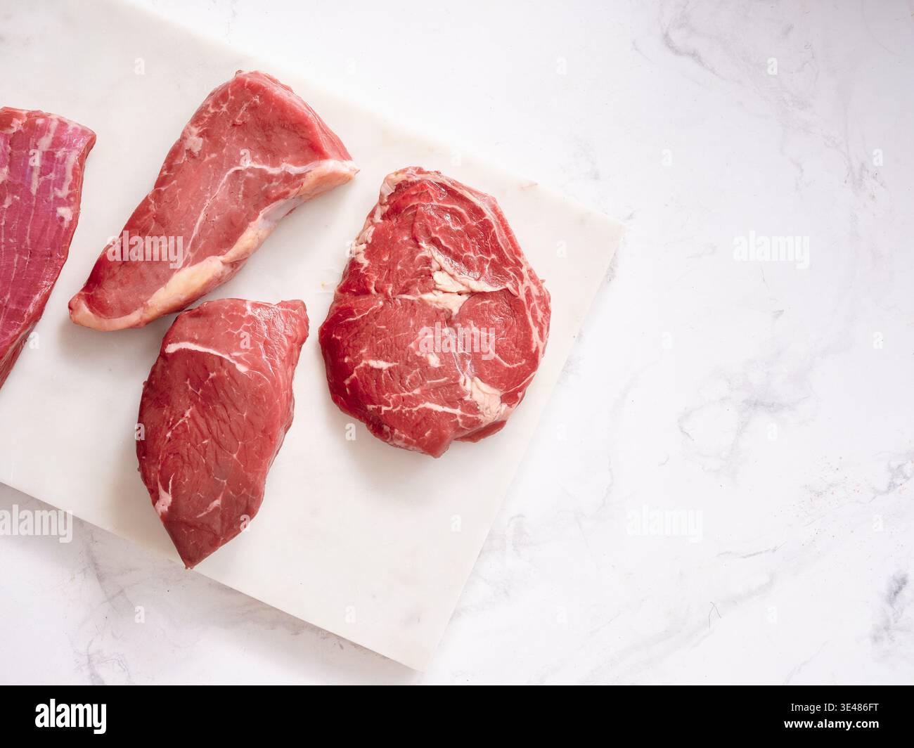 Mehrere rohe Rindfleischstücke werden auf einer weißen Oberfläche angezeigt. Zu den Aufschnitten gehören Rib-Eye, Roastbeef, Flanke und Rumpsteak, die zum Kochen zubereitet werden. Stockfoto