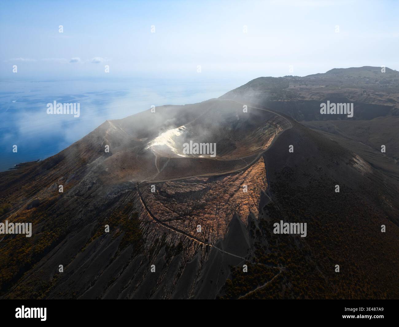 Aus der Vogelperspektive des Vulkankraters der Insel Vulcano auf den Äolischen Inseln mit Dampf, der vom Rand steigt und das blaue Meer im Hintergrund in Sicil Stockfoto