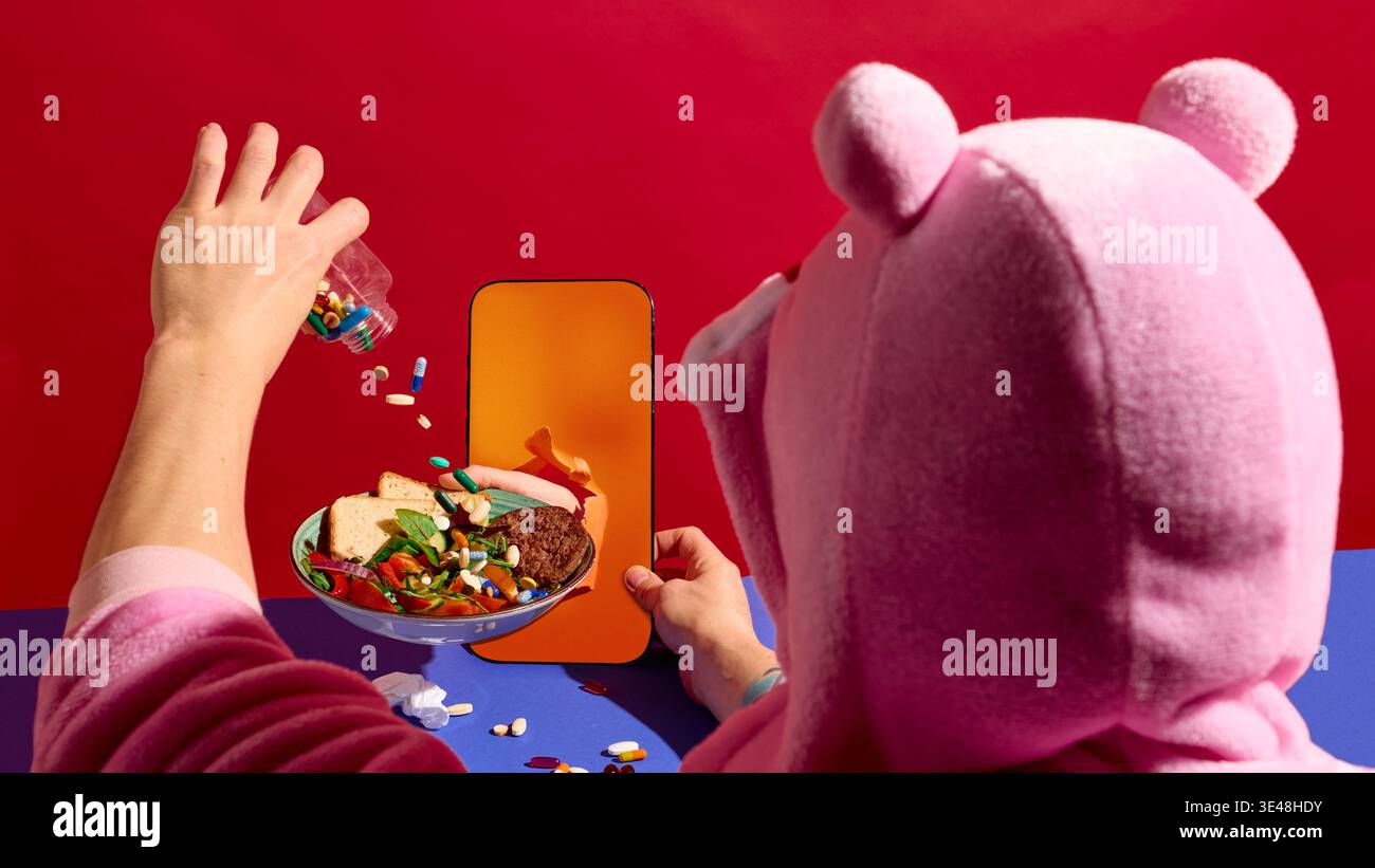 Person, die Pillen auf eine gesunde Mahlzeit vom Smartphone-Bildschirm in farbenfroher Einrichtung gießt. Stockfoto