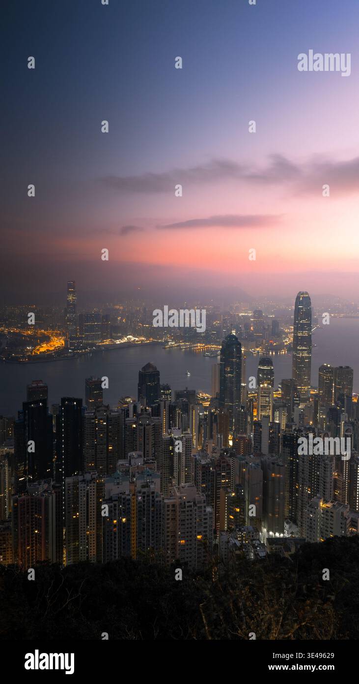Blick auf die beleuchtete Skyline und den Victoria Harbour mit Wolkenkratzern unter einem violetten Sonnenuntergang in Hongkong. Stockfoto