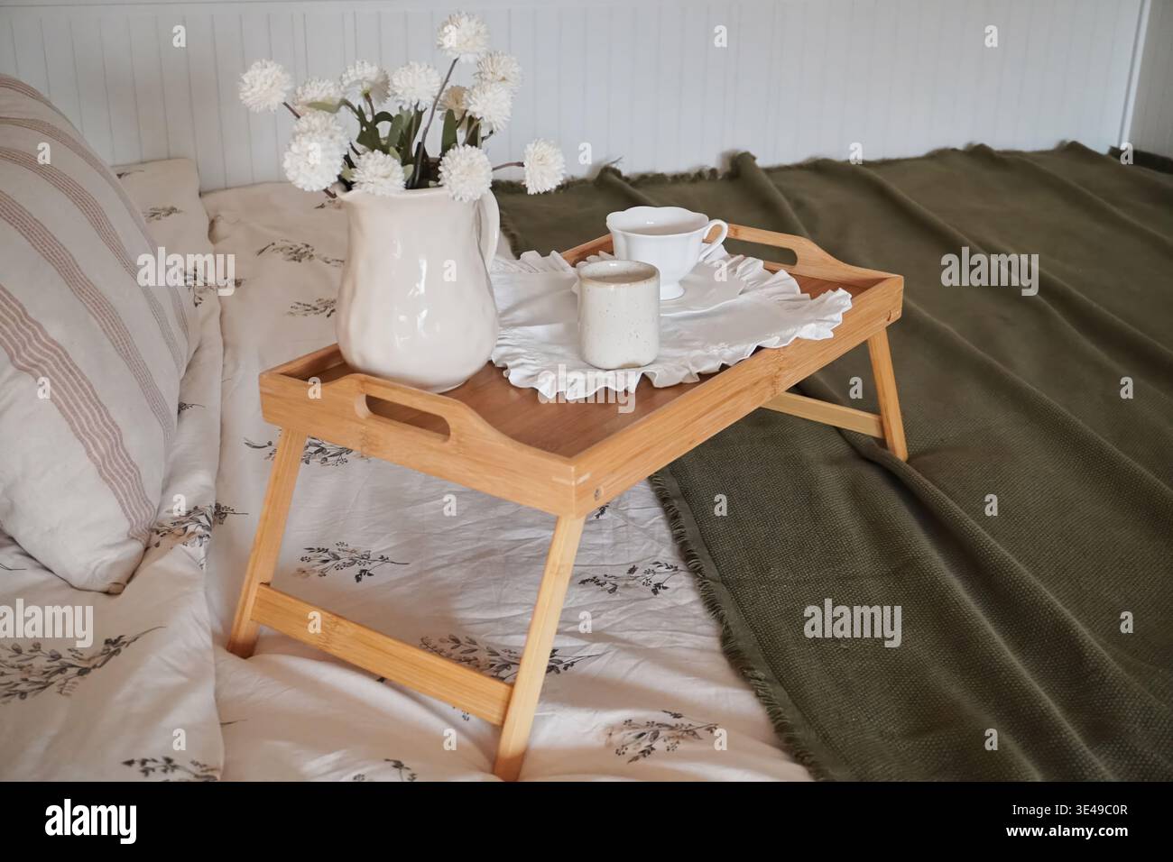 Ein gemütliches Frühstückstablett mit Blumen und Getränken auf einem Bett, umgeben von weichen Textilien Stockfoto