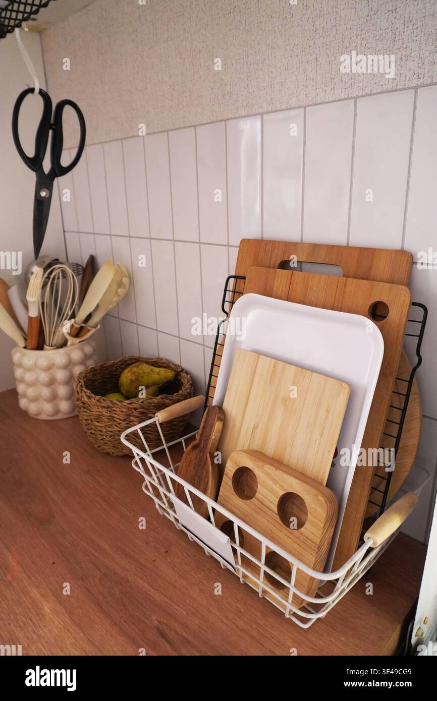 Organisierte Küchenutensilien und Schneidebretter in einem modernen Dekorationskorb Stockfoto