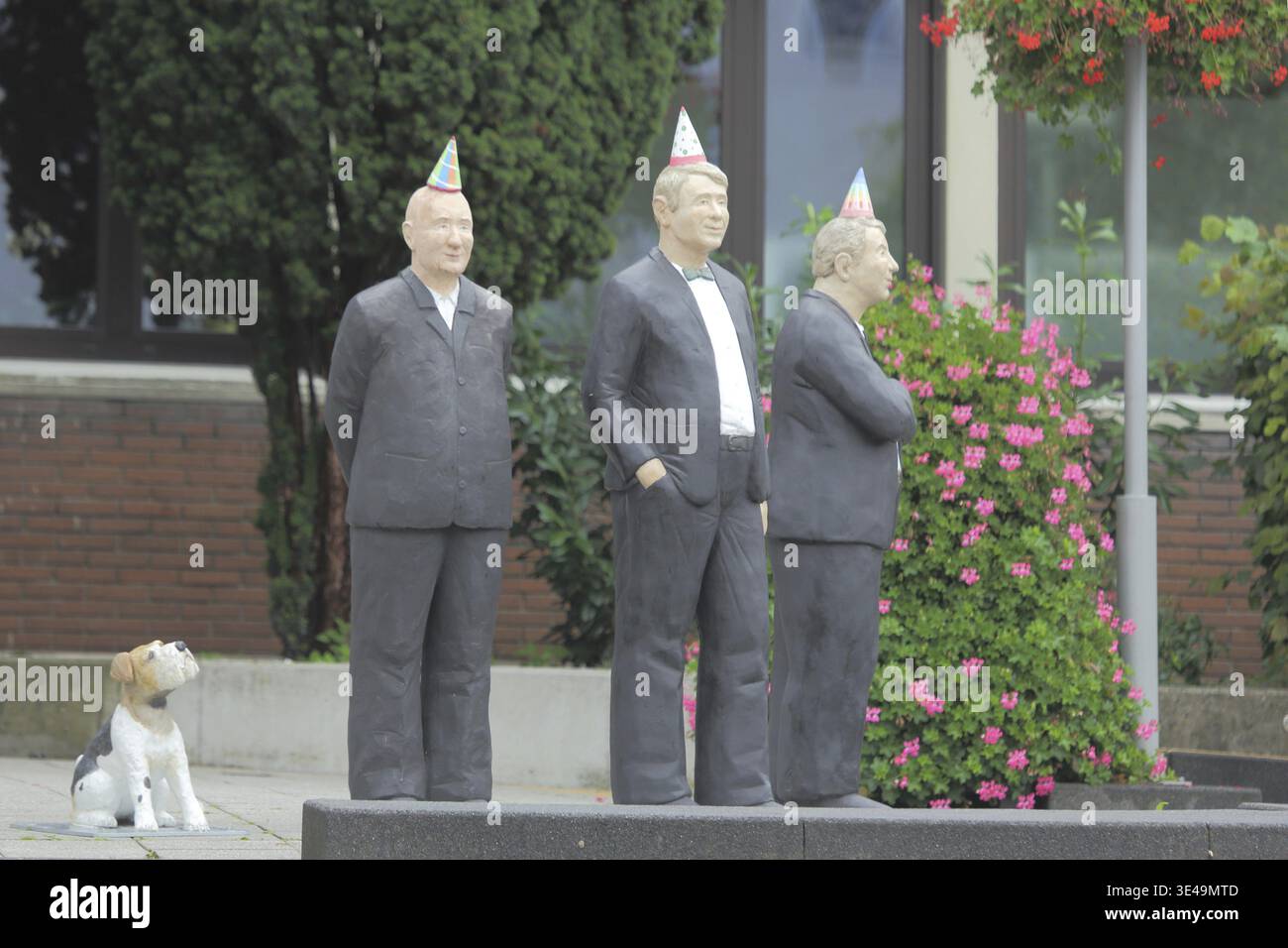 Ernst of Life Skulptur von Christel Lechner 2021, drei stehende Männer in Anzügen, bunter Hut, Hundefigur, humorvoll, lustig, moderne Kunst, lebensgroß, alles Stockfoto