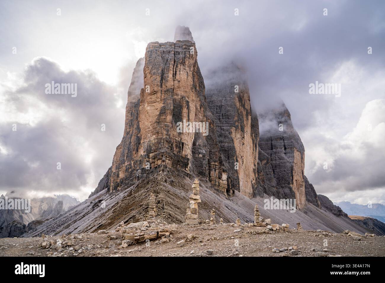 Flacher Blick auf die ikonischen Gipfel der drei Zinnen von Lavaredo, die in Nebel gehüllt sind. Im Vordergrund steinhügel auf kargem, felsigem Gelände. Ein dramatisches und s Stockfoto