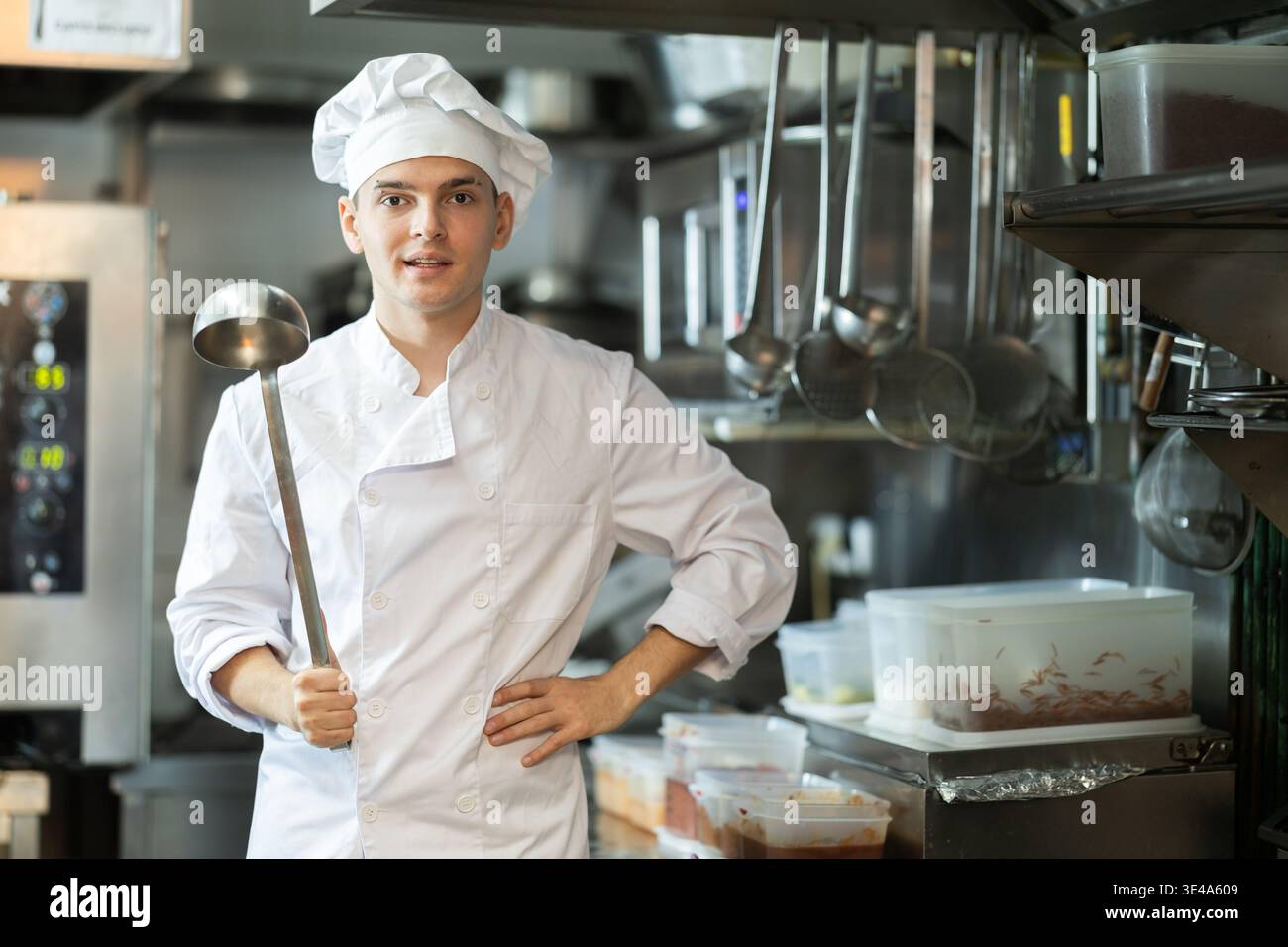 Junge männliche Köchin in Uniform stehend mit Schaufel in der Hand Stockfoto