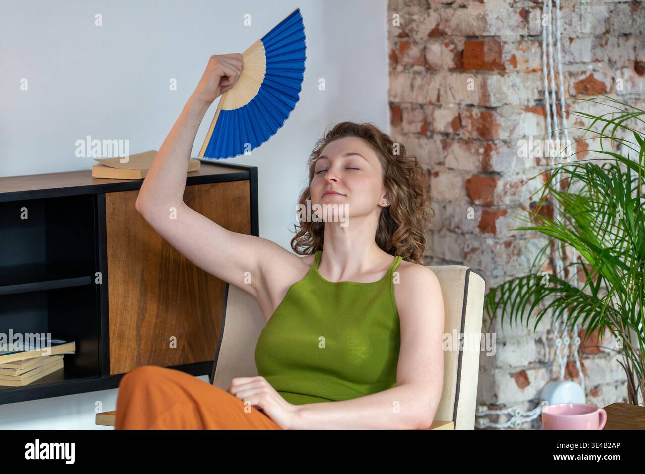 Eine glückselige, ruhige Frau mit geschlossenen Augen kühlt sich mit einem Handventilator ab. Machen Sie eine Pause vom hektischen Leben zu Hause Stockfoto