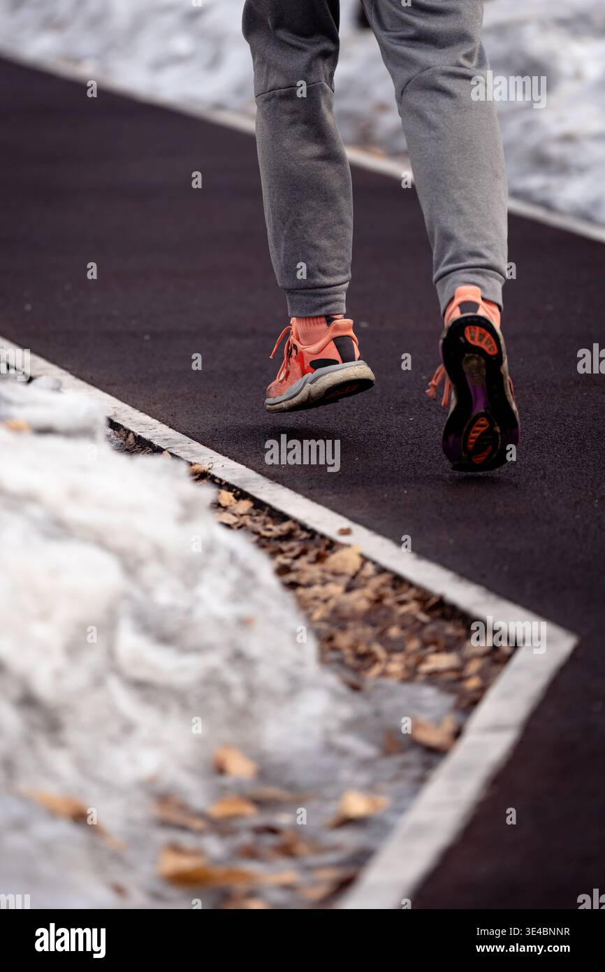 Ein Läufer in heller Sportausrüstung joggt auf einem freigelegten Weg, umgeben von Winterschnee Stockfoto