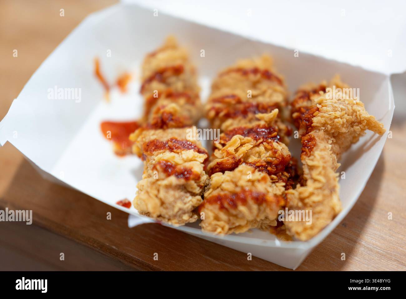 Knusprig gebratene Hähnchenstreifen mit roter Sauce in Papierkarton auf Holztisch, amerikanisches Fast Food, USA Stockfoto