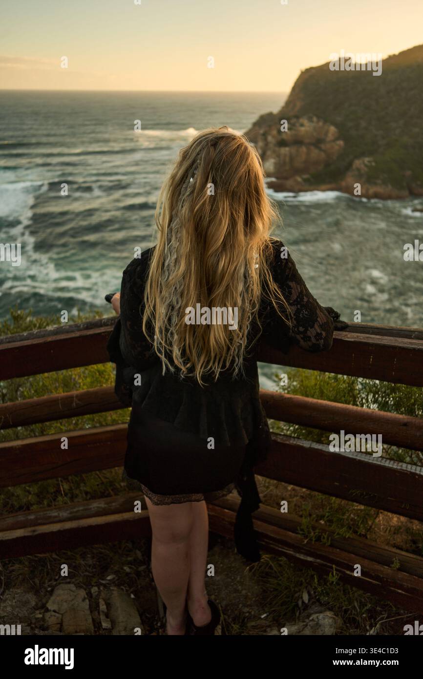Frau Blickt Auf Die Küste. Weibliche Figur Beobachtet Stürmische Wellen Gegen Die Rocky Shoreline Bei Sonnenuntergang Stockfoto