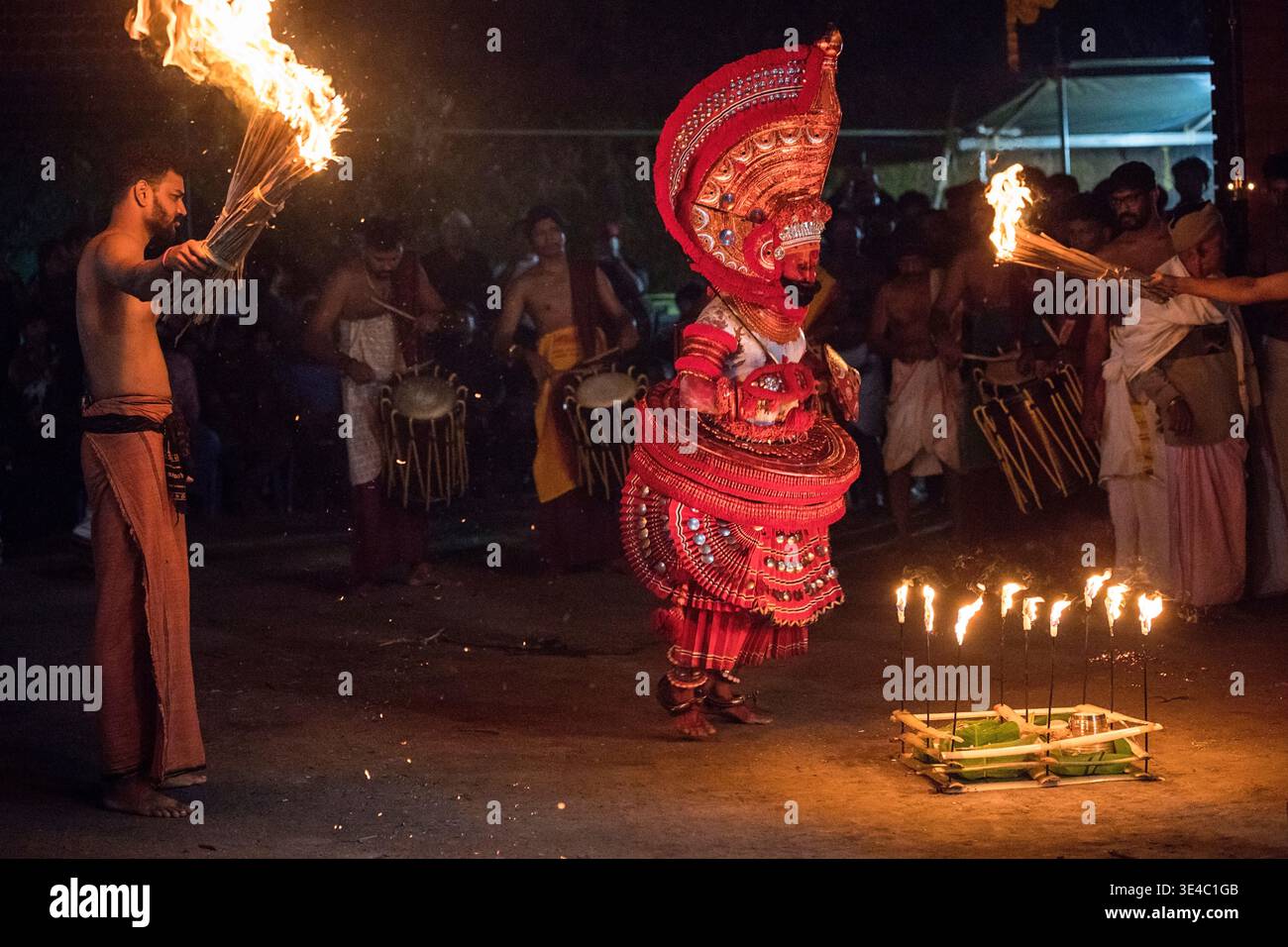 Theyyam-Darsteller tanzt mit Feuerfackeln und traditionellen Trommlern in der Nacht, Kerala, Indien Stockfoto