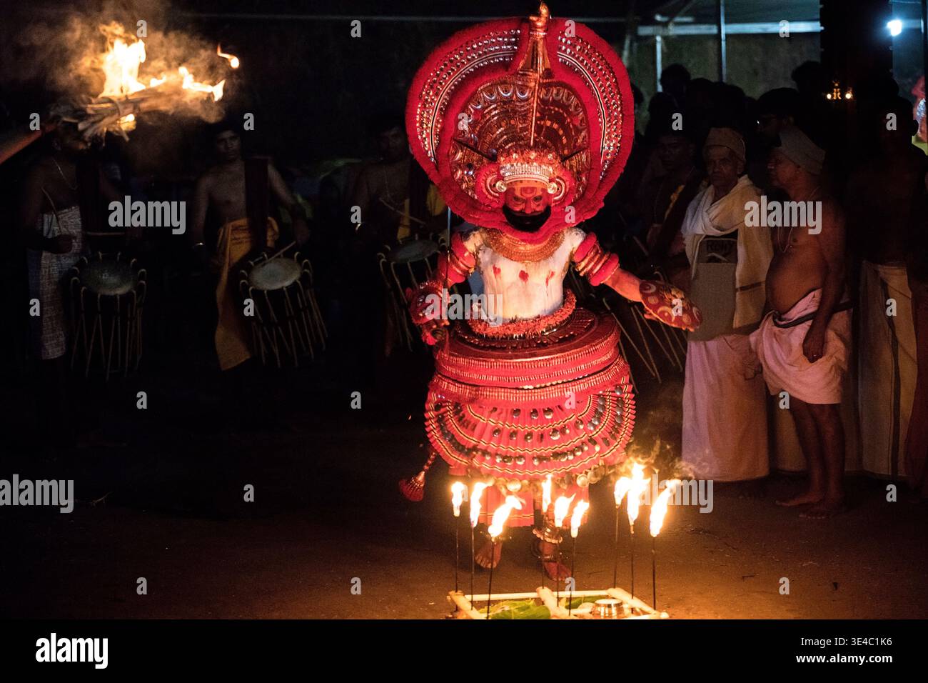 Theyyam-Darsteller tanzt mit Feuerfackeln und traditionellen Trommlern in der Nacht, Kerala, Indien Stockfoto