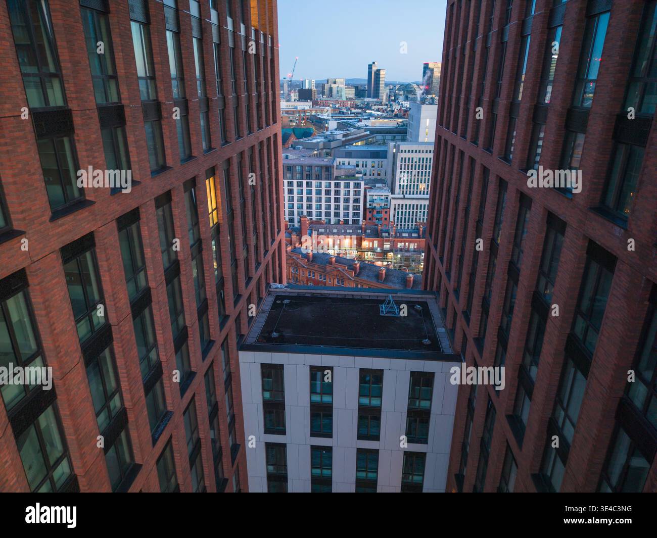Eine beeindruckende Luftperspektive mit Blick zwischen zwei modernen Backsteinhochhäusern in Richtung der Skyline der Stadt während der ruhigen Momente der Dämmerung. Stockfoto