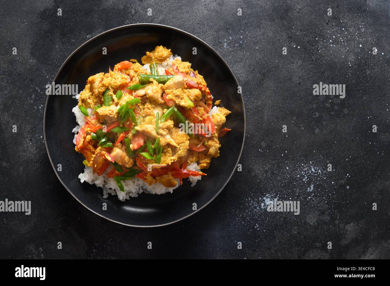 Thailändisches Frühstück Gai Pad Pongali mit Hühnchen, Eiern, scharfer, gelber thai-Currypaste, Tomaten, Reis in schwarzer Schüssel aus Wok. Nahaufnahme. Panasiatische Küche. Thailändisches Essen Gebraten. Stockfoto