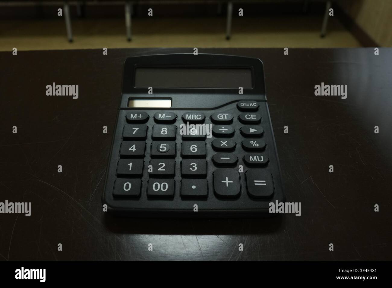 Der einfache schwarze Rechner befindet sich auf einer dunklen Holzoberfläche. Die Tasten sind für grundlegende mathematische Funktionen eindeutig gekennzeichnet. In diesem i sind keine Menschen oder Tiere zu sehen Stockfoto