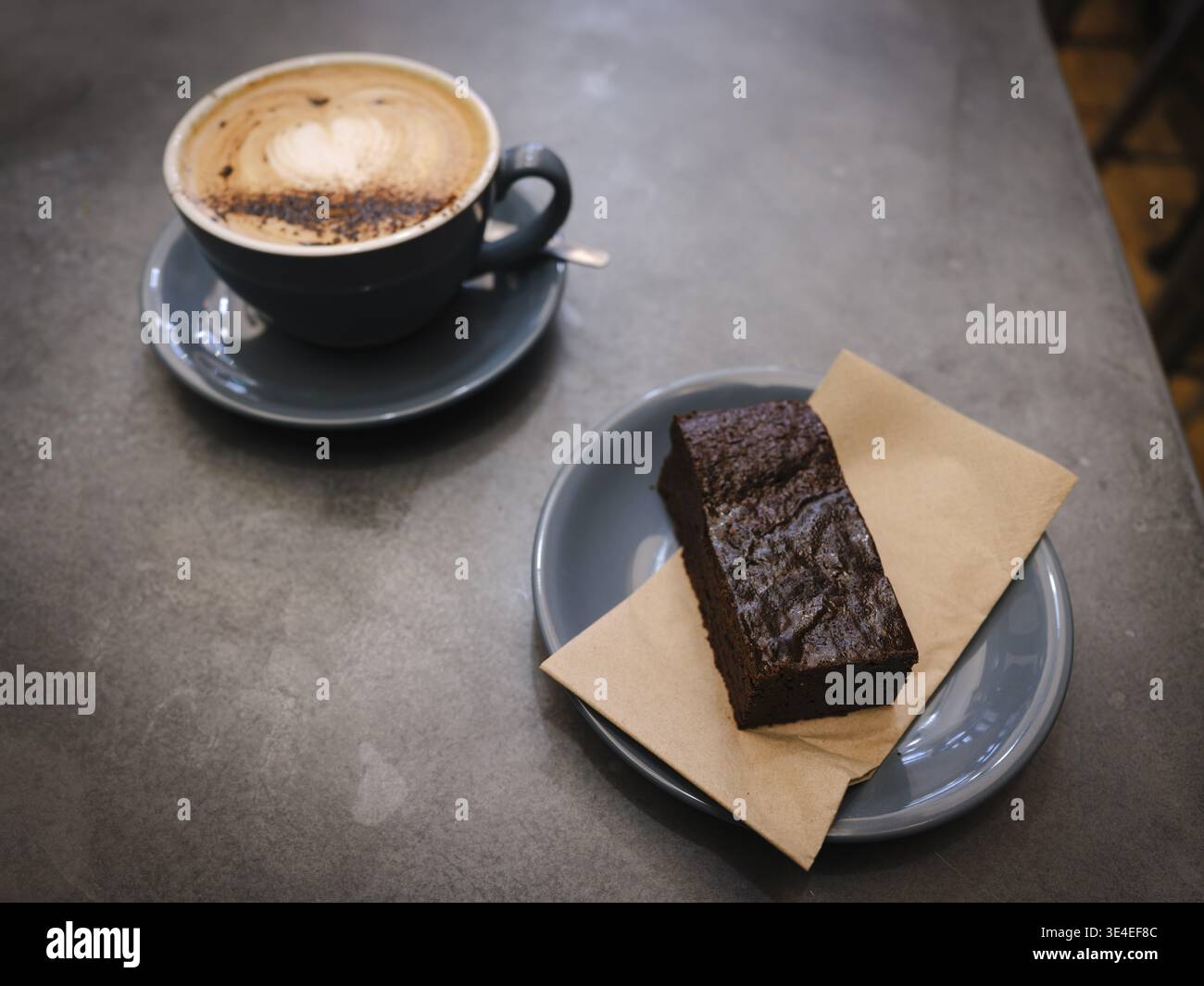 Cappuccino mit herzhafter Latte Art und Schokoladenbrownie auf dem Tisch im Cafe Coho in Brighton Stockfoto