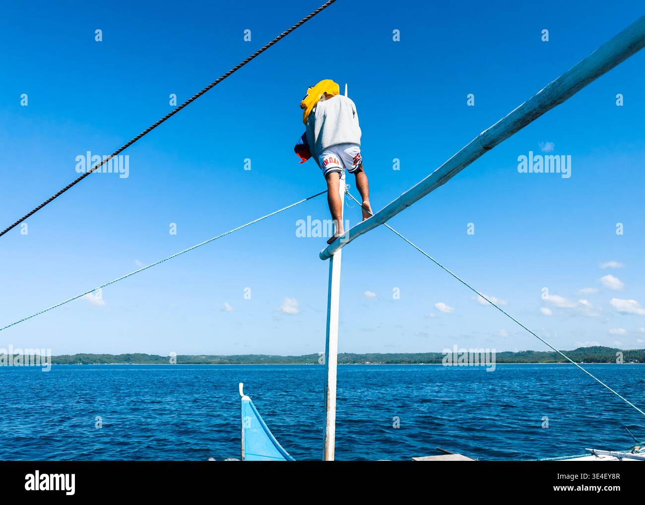 Walhai-Spotter balancieren auf einem Bootsmast in Donsol und suchen das Meer nach sanften Riesen unter einem klaren blauen Himmel - Smartphone-aufgenommenes Stockfoto