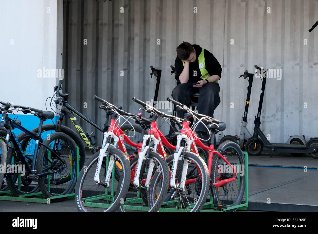 Ein junger Arbeiter sitzt in einem Container und ruht sich aus, während Fahrräder und Motorroller in der Nähe warten. Ukraine, Kiew, Expocenter der Ukraine, 27. März 2026 Stockfoto