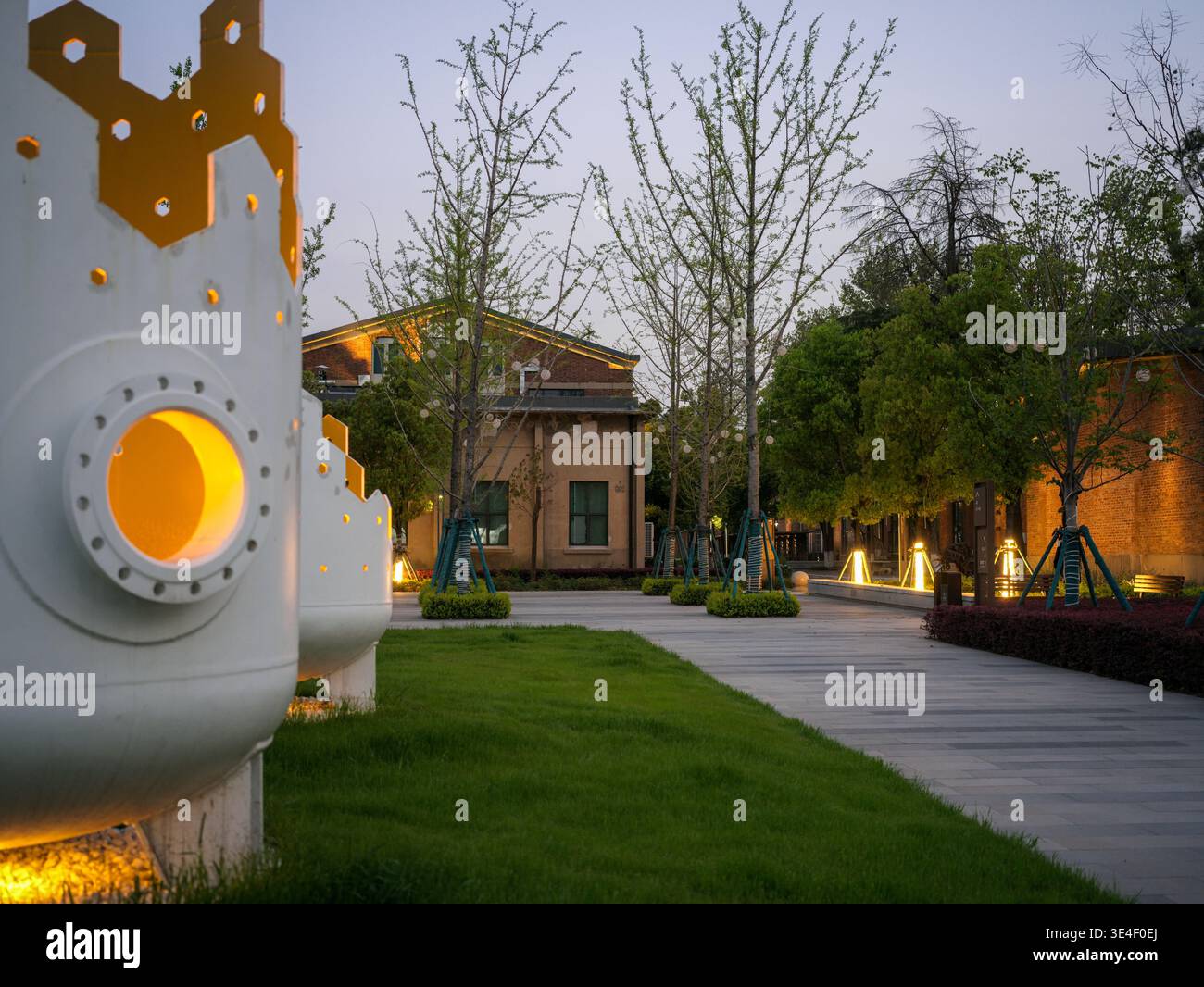 Wuhan, China - 5. April 2025: Nahaufnahme einer beleuchteten weißen zylindrischen Skulptur mit kreisförmiger Öffnung, die mit warmgelbem Licht in A leuchtet Stockfoto