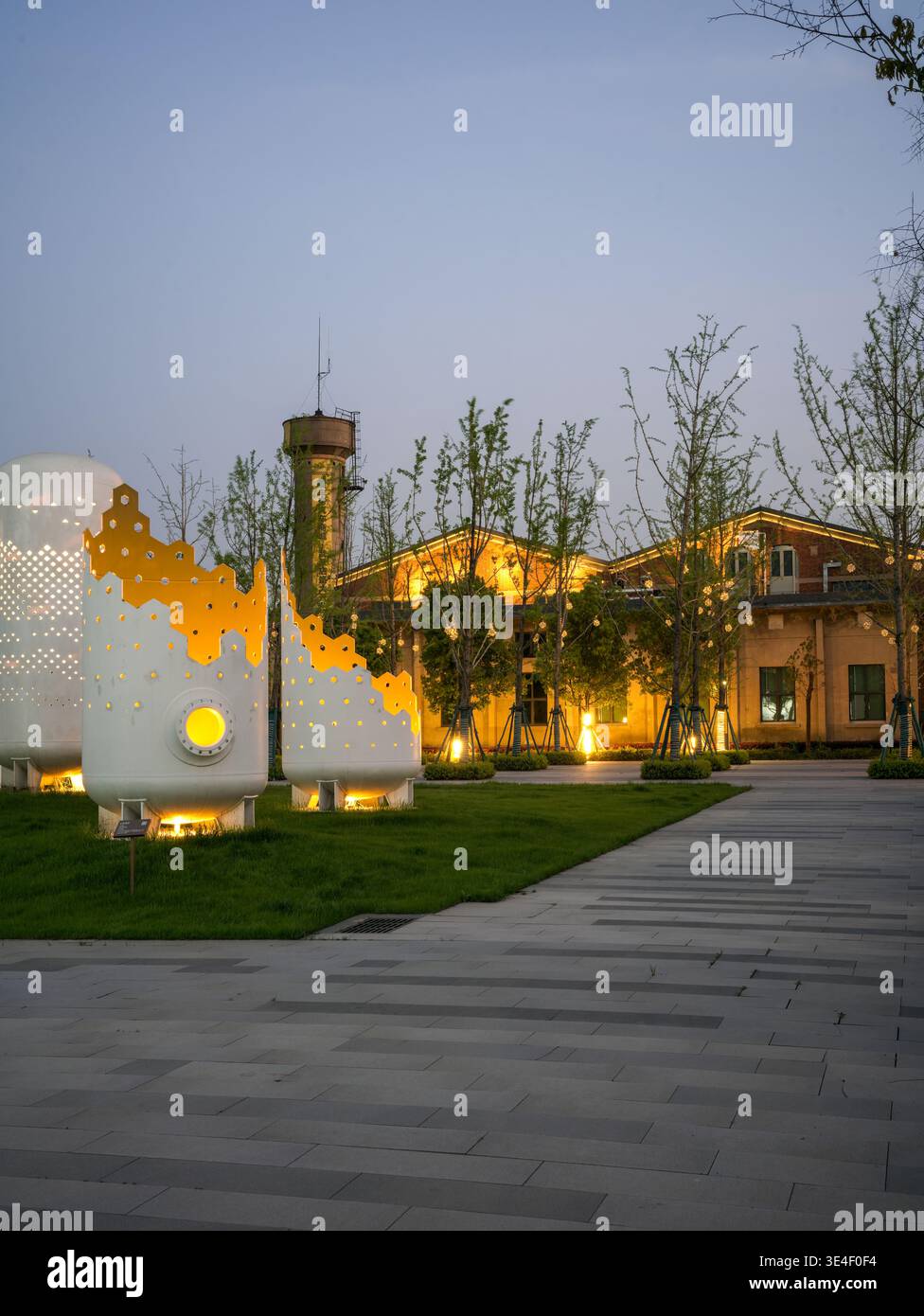 Wuhan, China - 5. April 2025: Öffentliche Parklandschaft mit beleuchteten weißen Skulpturen im industriellen Stil auf einem Rasen in der Abenddämmerung. Die Bilderfassung Stockfoto