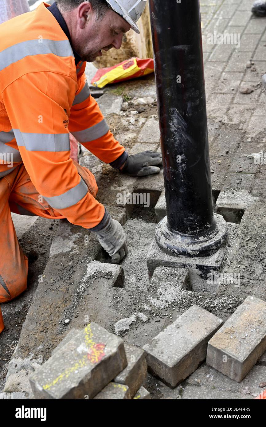 Arbeiter, der Pfosten in Straßenpflaster mit gut sichtbarer Kleidung installiert Stockfoto