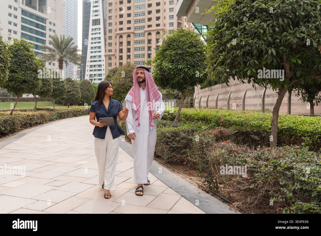Ein arabischer Geschäftsmann und eine asiatische Geschäftsfrau nehmen an einem Treffen teil, während sie in einer modernen Stadt spazieren gehen. Stockfoto
