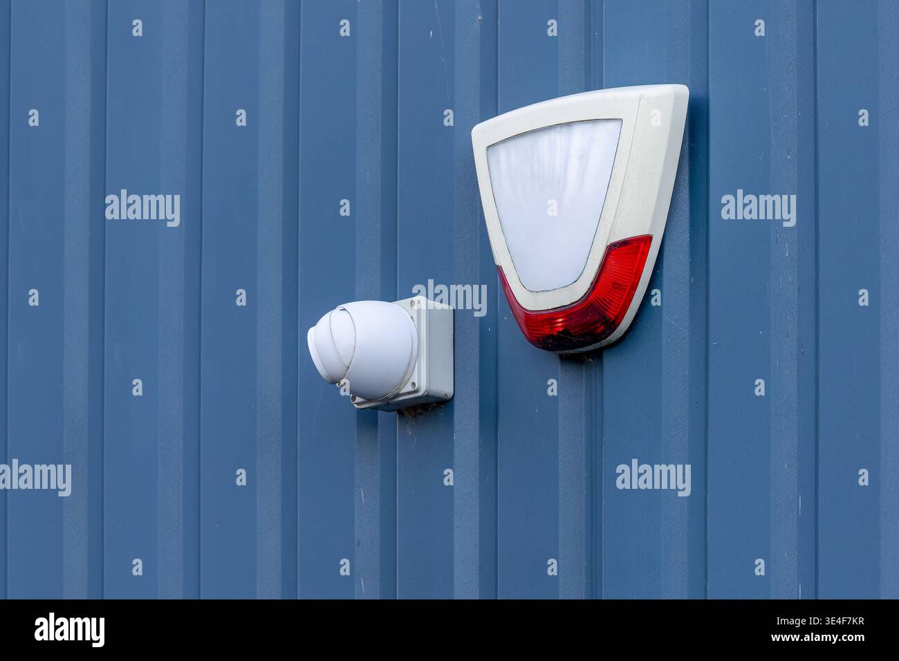 Weiße Dome-CCTV-Kamera und Alarmbox für Sicherheitssirene, montiert auf blauem Wellblech-Industriebau. Eigentumsschutz- und Überwachungskonzept Stockfoto