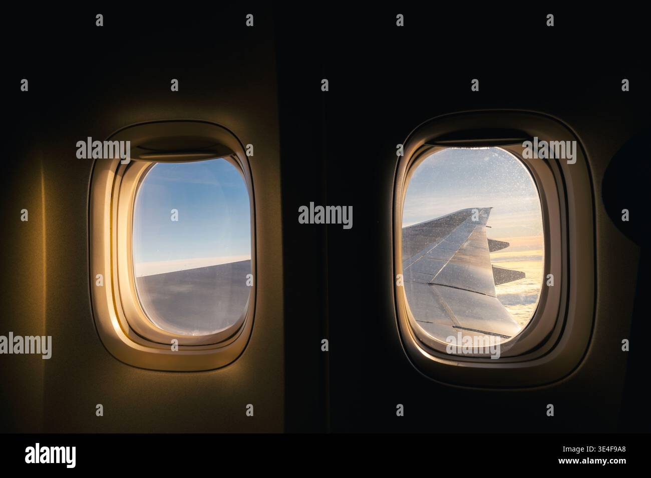 Blick durch das Flugzeugfenster mit dem Flugzeugflügel, der während des Fluges durch Sonnenaufgangslicht beleuchtet wird. Reiseatmosphäre, Luftfahrt, friedlich mehr Stockfoto