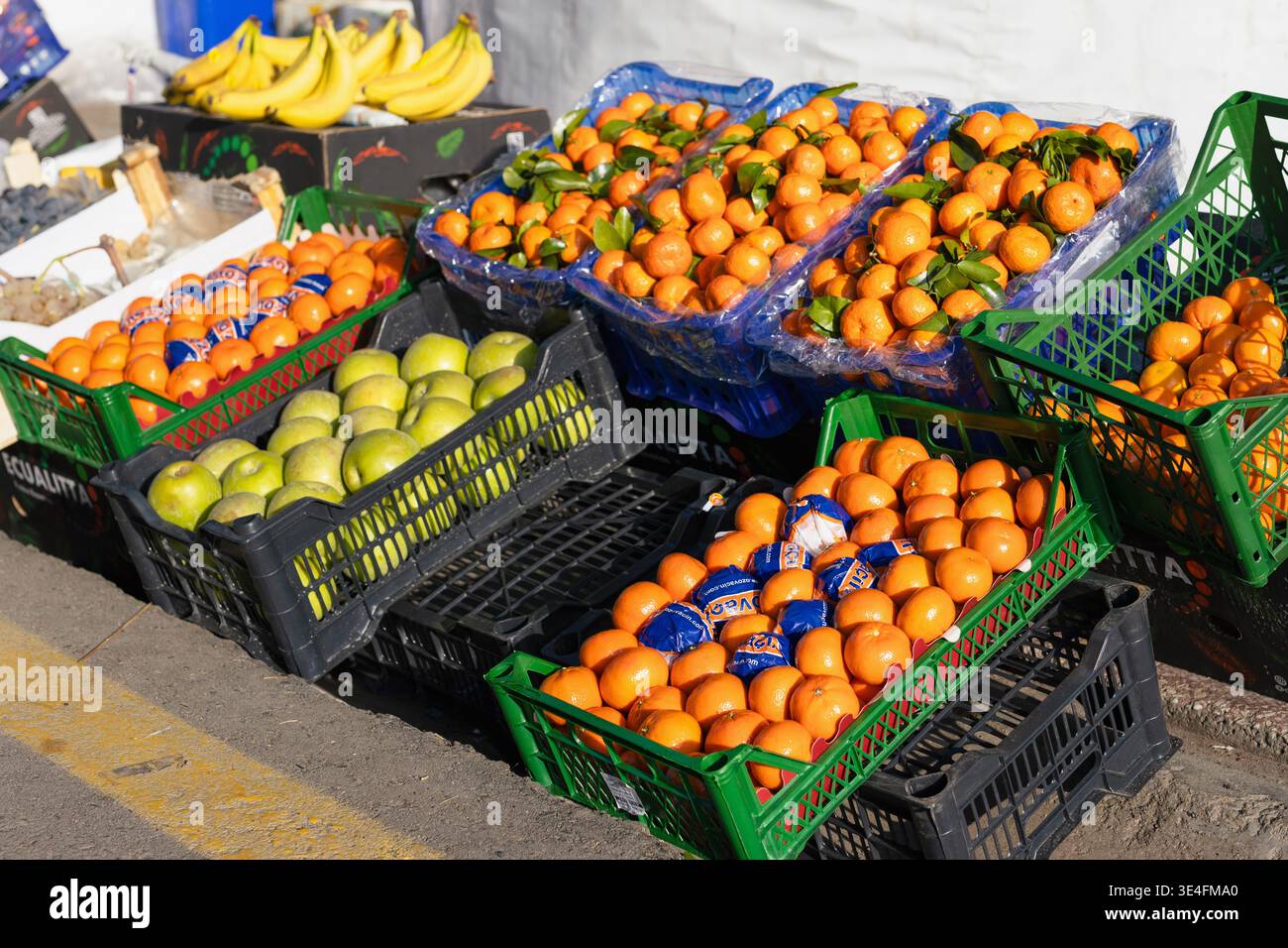 Sonniger Obstmarkt auf der Straße mit frischen Orangen, Mandarinen und grünen Äpfeln in bunten Plastikkisten. Lebhafte Basarszene im Freien in hellem Licht Stockfoto