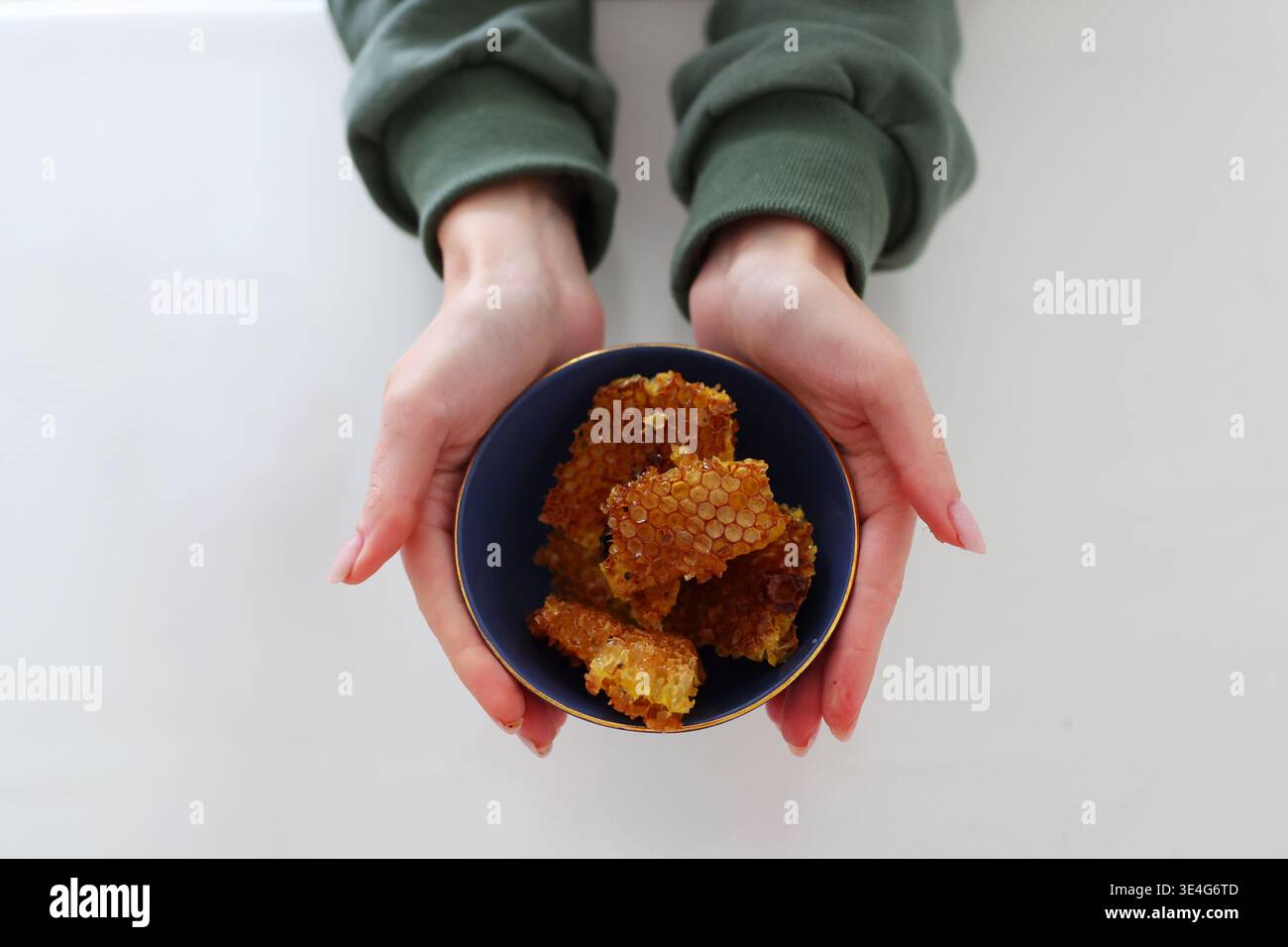 Hände halten Schüssel mit Wabe, natürlichem Bio-Honig und gesundem Lebensmittelkonzept auf sauberem minimalem Hintergrund. Stockfoto
