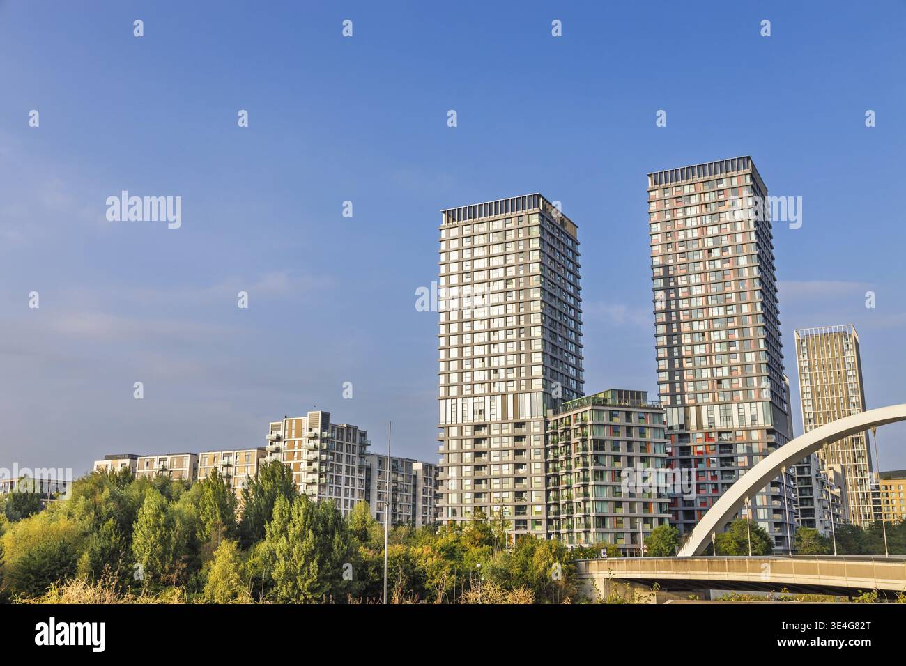 Elegante Glastürme ragen über einen üppigen Stadtpark und eine Bogenbrücke Stockfoto