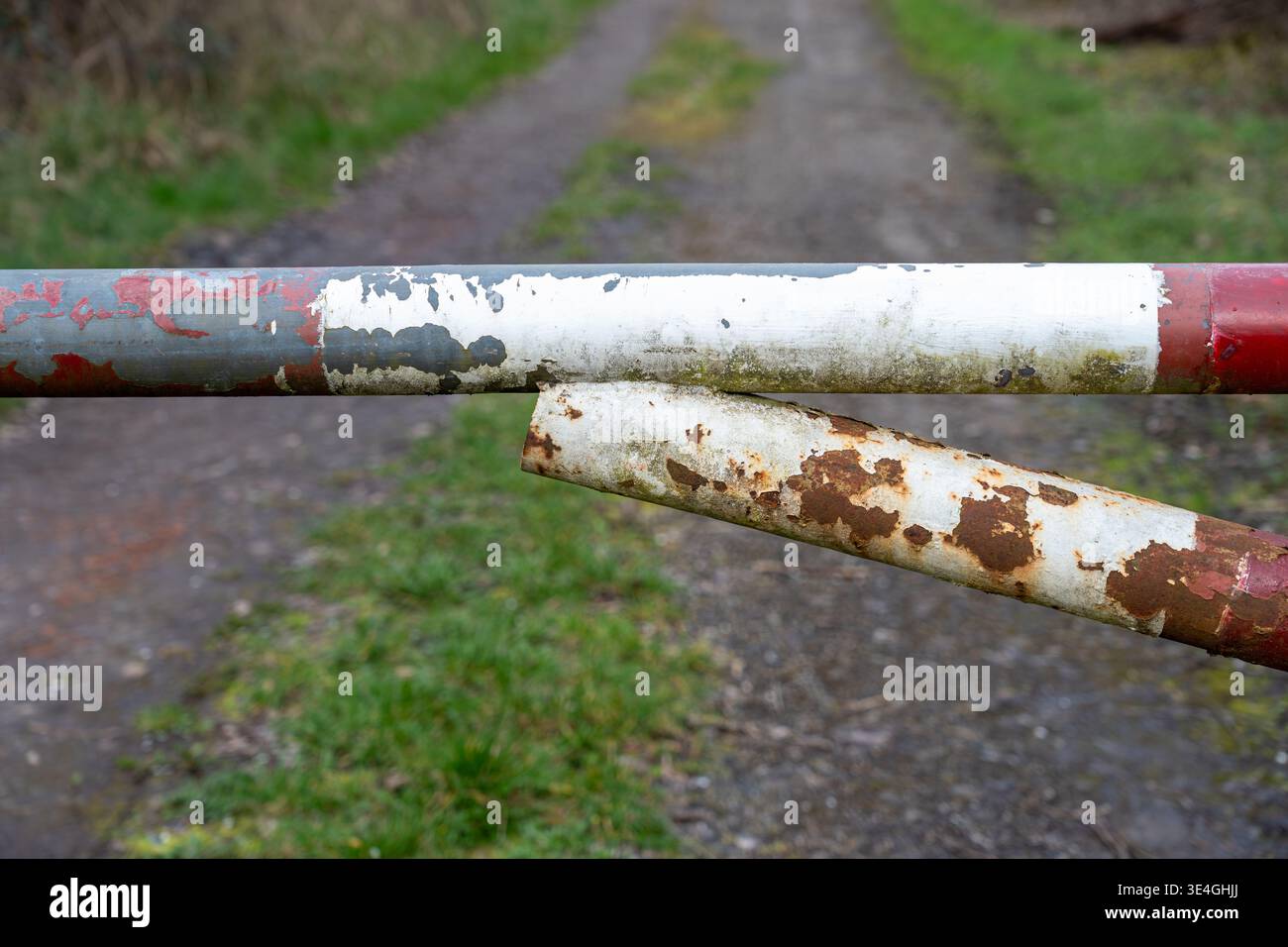 Detaillierte Ansicht eines verrotteten, lackierten Torarms aus Stahl über einer sanft verschwommenen ländlichen Feldbahn. Stockfoto