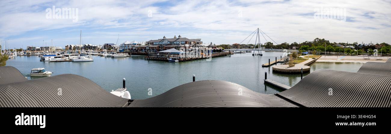 Breiter Panoramablick auf die Küste von Mandurah und den Yachthafen mit zahlreichen Booten und Yachten, die an hölzernen Piers vertäut sind, moderne Gebäude mit markantem Bogen Stockfoto