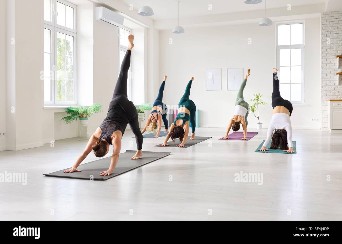 Yoga-Klasse hebt Beine in dreibeiniger Hundehaltung in einem hellen Studio-Innenraum Stockfoto