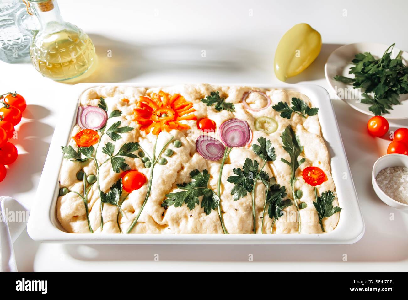 Hausgemachte italienische Focaccia auf einem Backblech, gestylt als Blumengemälde mit Petersilie, Zwiebeln, Tomaten, Erbsen und Pfefferscheiben. Helle Lebensmittelfotografie auf einem Whi Stockfoto