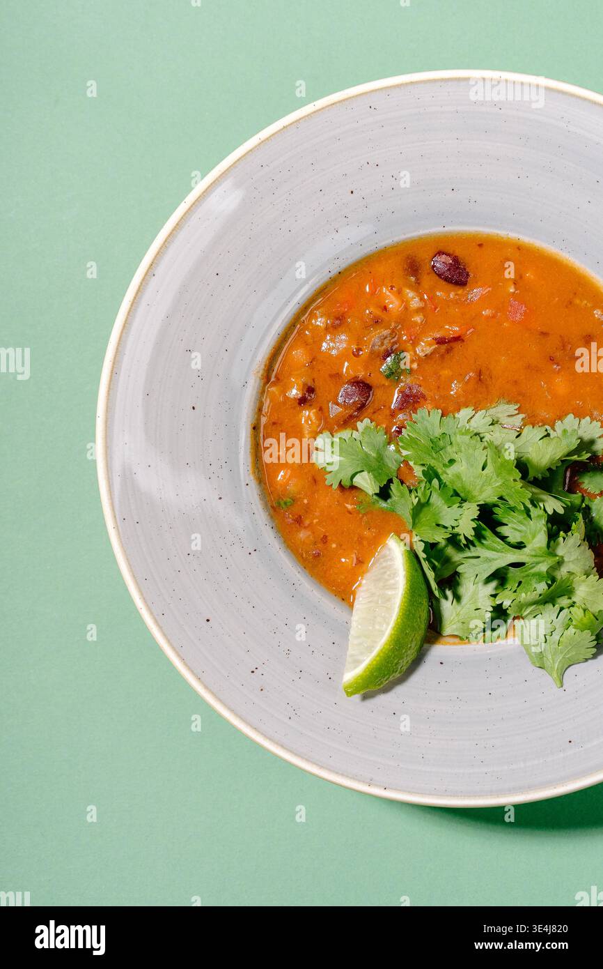 Foto von mexikanischer Tomatensuppe mit roten Bohnen und Chorizo, garniert mit Koriander und Limette. Behagliches Gericht im Restaurant-Stil mit rauchigen Gewürzen, s Stockfoto