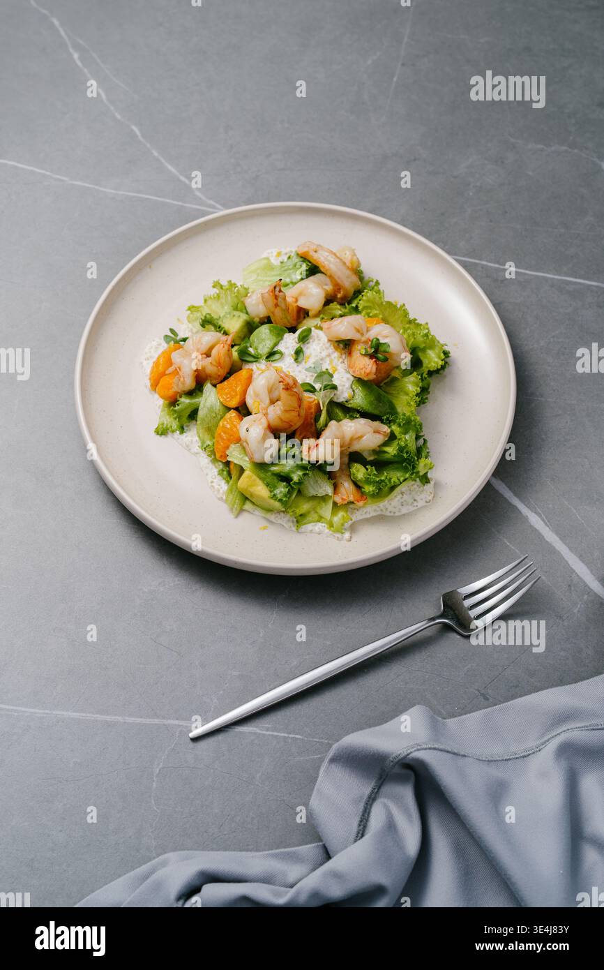 Frischer Salat mit frittierten Tigergarnelen, Orangensegmenten, Avocado, knusprigem Salat und Mikrogrün, garniert mit cremiger Zitronensauce, Frischkäsenoten und Stockfoto