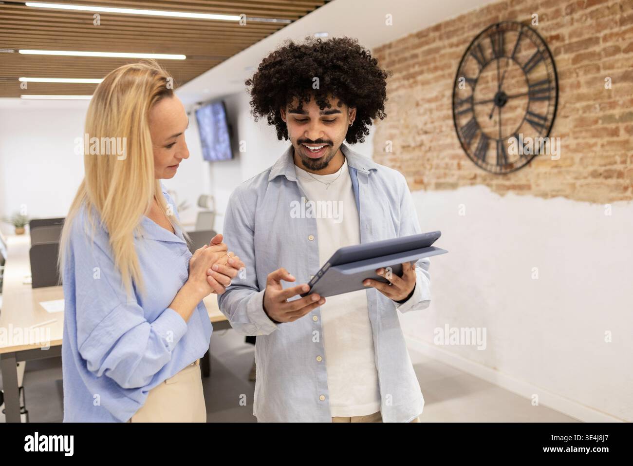 Lateinischer Mann und weibliche Kollegin prüfen Daten auf einem Tablet in einem modernen Coworking-Büro und diskutieren Projektideen und Teamarbeit in einem hellen, offenen Design Stockfoto