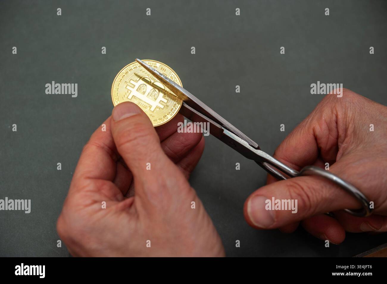 Hände schneiden eine Bitcoin-Münze mit einer Schere ab, die Kryptowährungsverlust, Risiko und finanzielle Unsicherheit auf digitalen Märkten symbolisiert Stockfoto