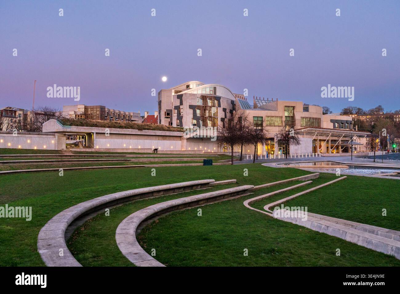 Mondlicht-Blick auf das schottische Parlamentsgebäude und das gestaltete Amphitheater im Holyrood Park, Edinburgh, mit geschwungenen Steinterrassen und reflektierendem Pool Stockfoto