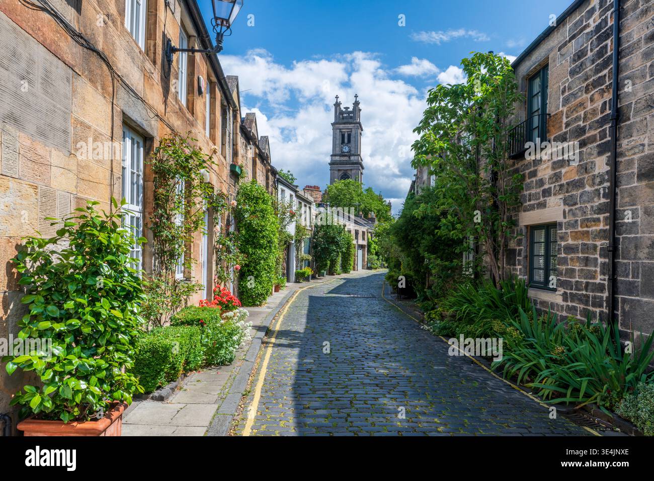 Sonniges Kopfsteinpflaster Circus Lane in Stockbridge, gesäumt von georgianischen Stadthäusern, Topfpflanzen und Kletterweben, führt zu einem historischen Kirchturm Stockfoto