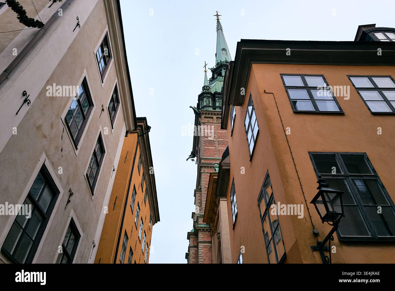 Lebhafte historische Gebäude säumen einen hohen, verwitterten Turm. Sonnenlicht strahlt aus alten Steinen und bemalten Fassaden. Fenster reflektieren Himmel und Schatten sanft. Stockfoto