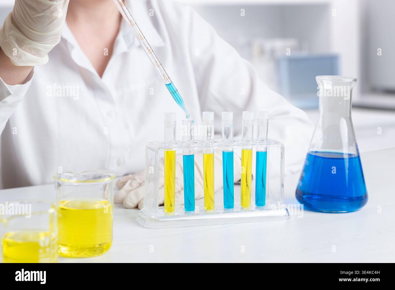 Wissenschaftler mit Pipette zum Umfüllen blauer Flüssigkeit in Reagenzgläser, Laborversuche und chemische Analysen in kontrollierter Umgebung Stockfoto