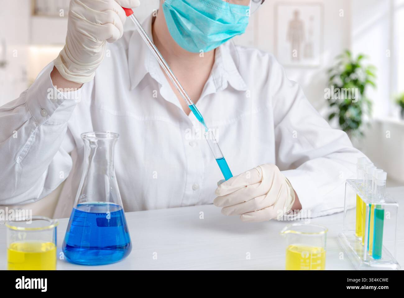 Labortechniker mit Pipette zum Umfüllen der blauen Flüssigkeit in Reagenzgläser, chemische Forschung und wissenschaftliche Experimente in kontrollierter Umgebung Stockfoto